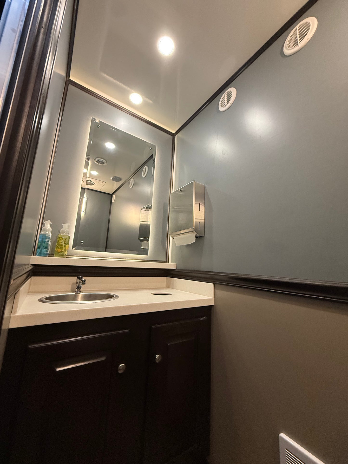 Luxury restroom trailer interior with sink, mirror, and vanity cabinet, featuring modern finishes for event rentals in North Carolina.