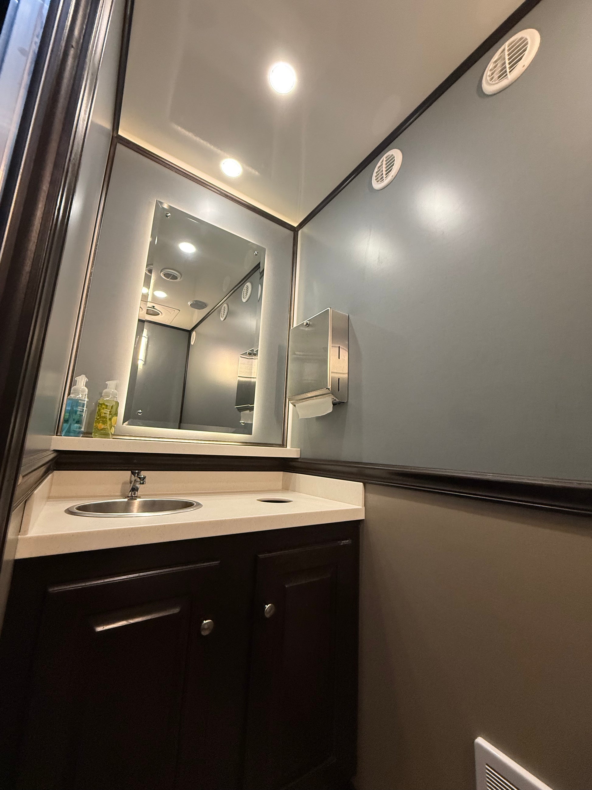 Luxury restroom trailer interior with sink, mirror, and vanity cabinet, featuring modern finishes for event rentals in North Carolina.