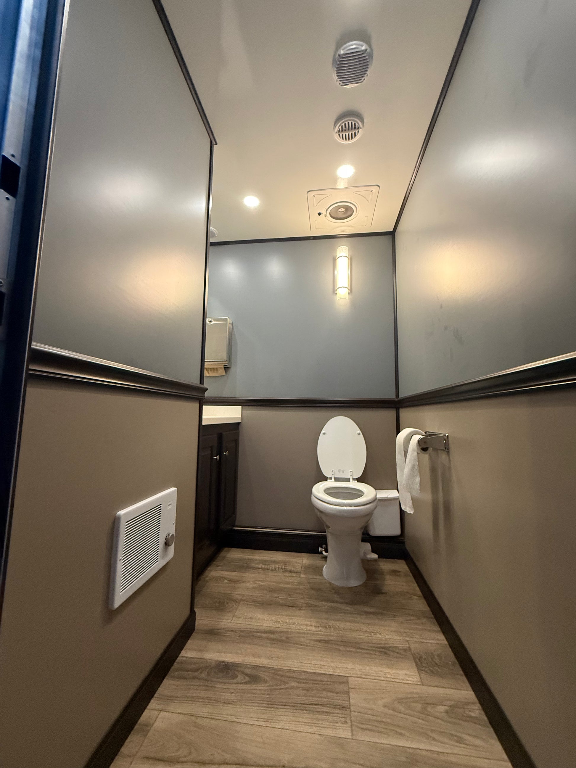 Luxury restroom trailer interior with toilet, vanity, modern lighting, and wood-look flooring, available for wedding and event rentals in North Carolina.