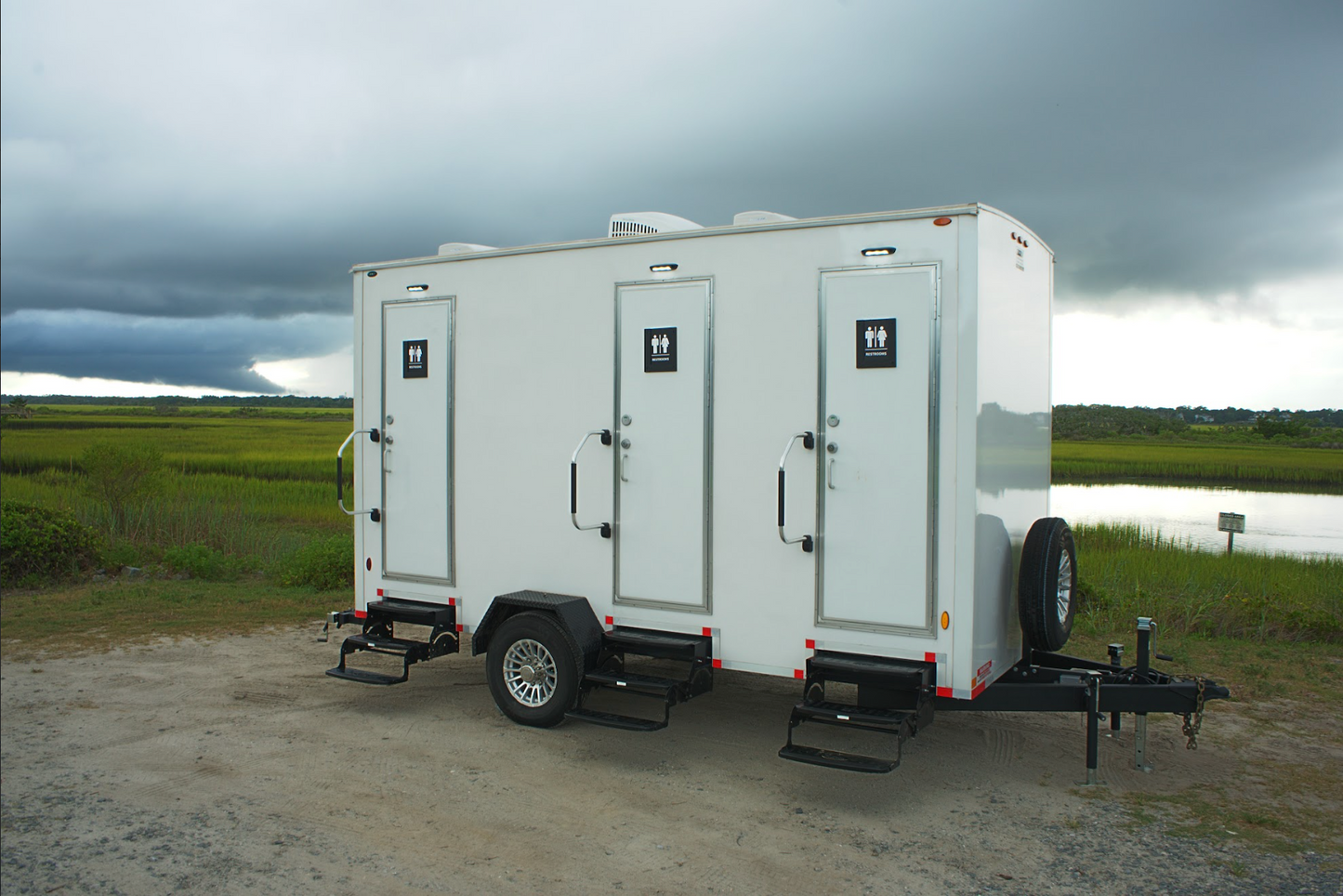 3-stall luxury restroom trailer rental parked outdoors near Wilmington, NC – portable restroom unit with private entrances and steps, ideal for weddings and events.