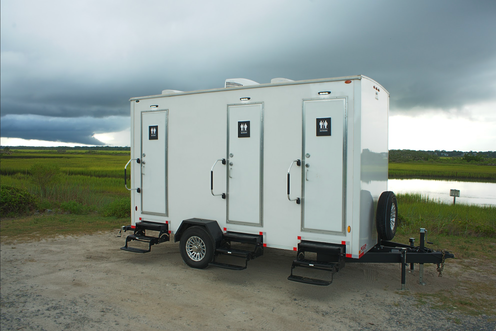 3-stall luxury restroom trailer rental parked outdoors near Wilmington, NC – portable restroom unit with private entrances and steps, ideal for weddings and events.